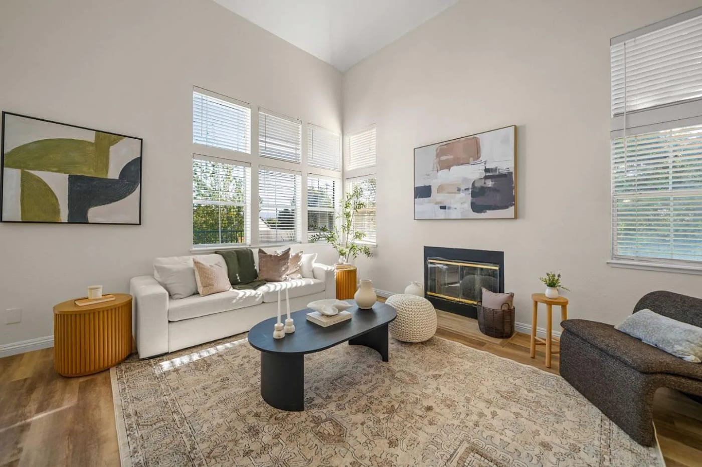 Staged living room with a vaulted ceiling, white sofa, black round coffee table, and a fireplace