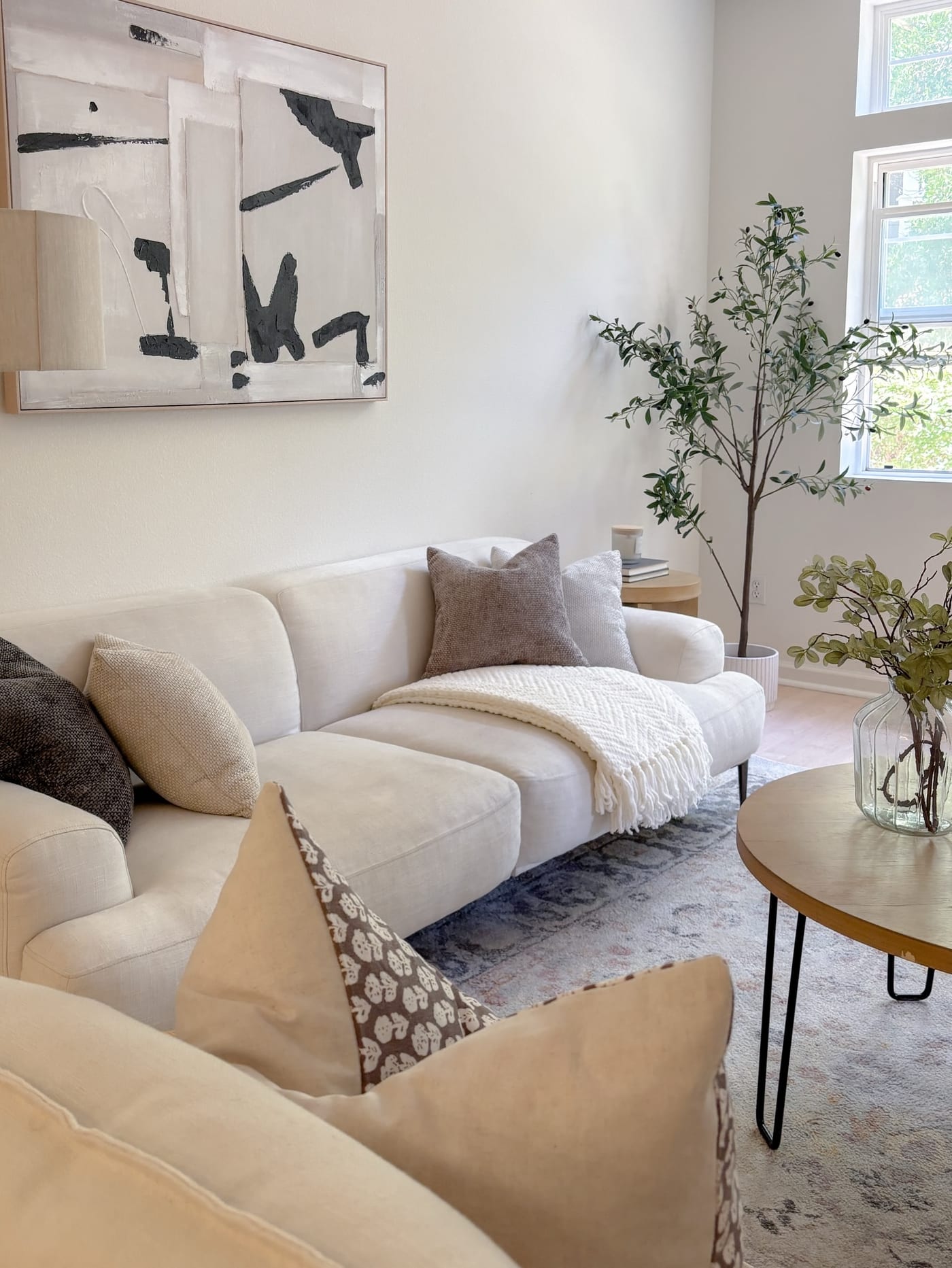 Staged living room with a cream sofa, olive tree, and a black-and-white abstract canvas
