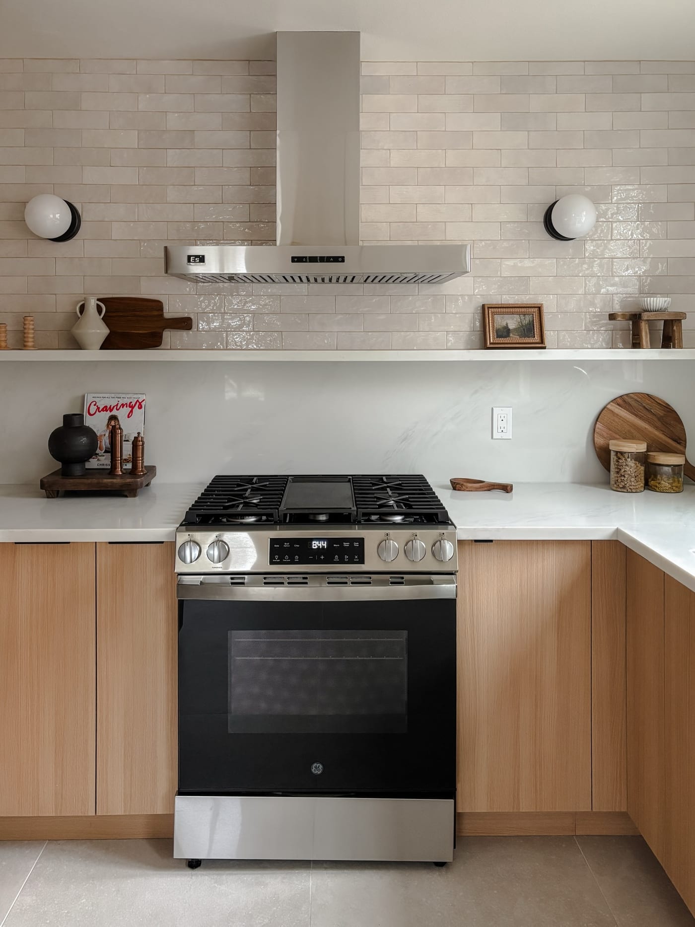 Staged kitchen with a stainless gas range, white subway tile, and light oak cabinets