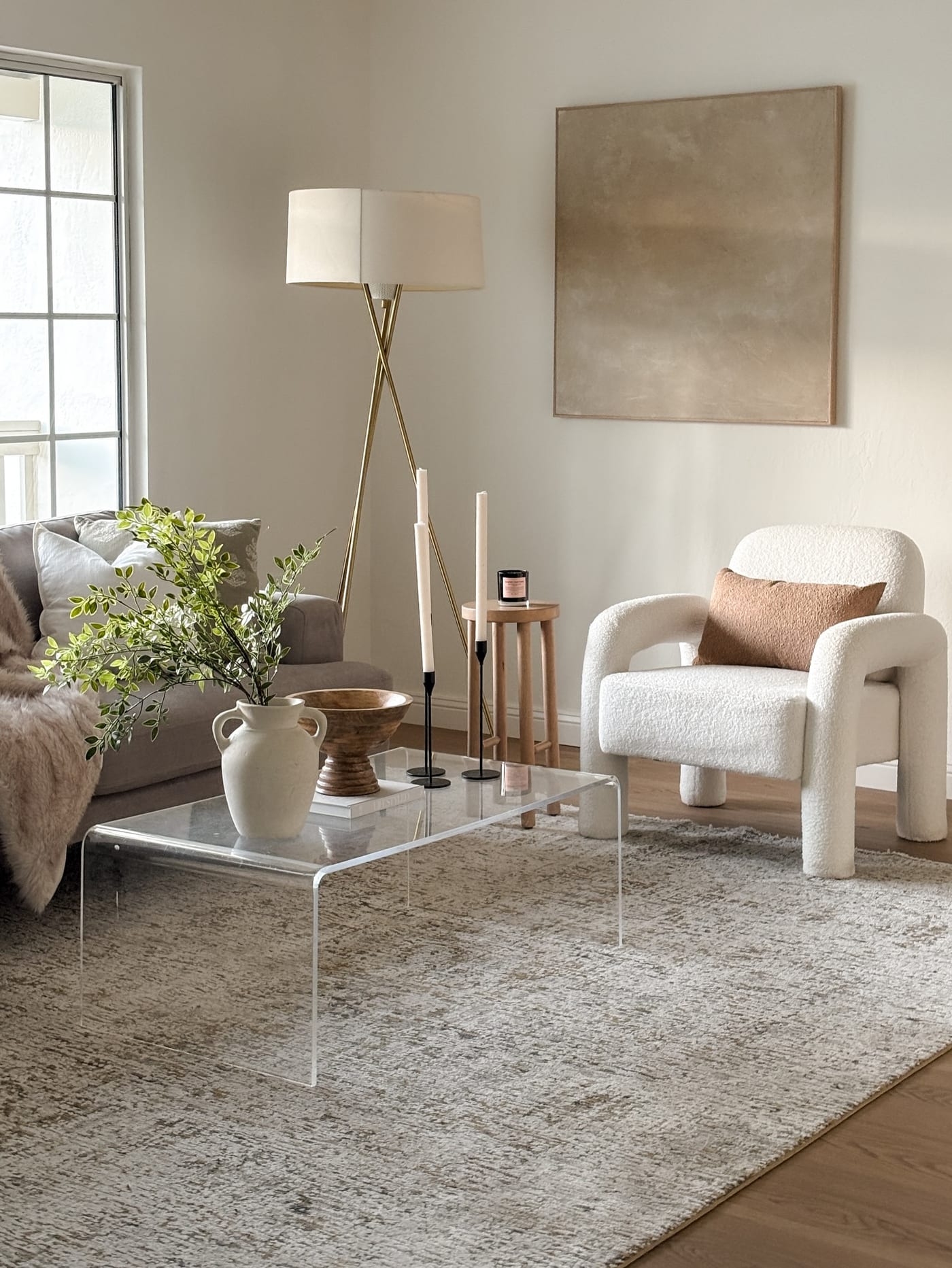 Staged living room with an acrylic coffee table, boucle accent chair, and brass tripod lamp