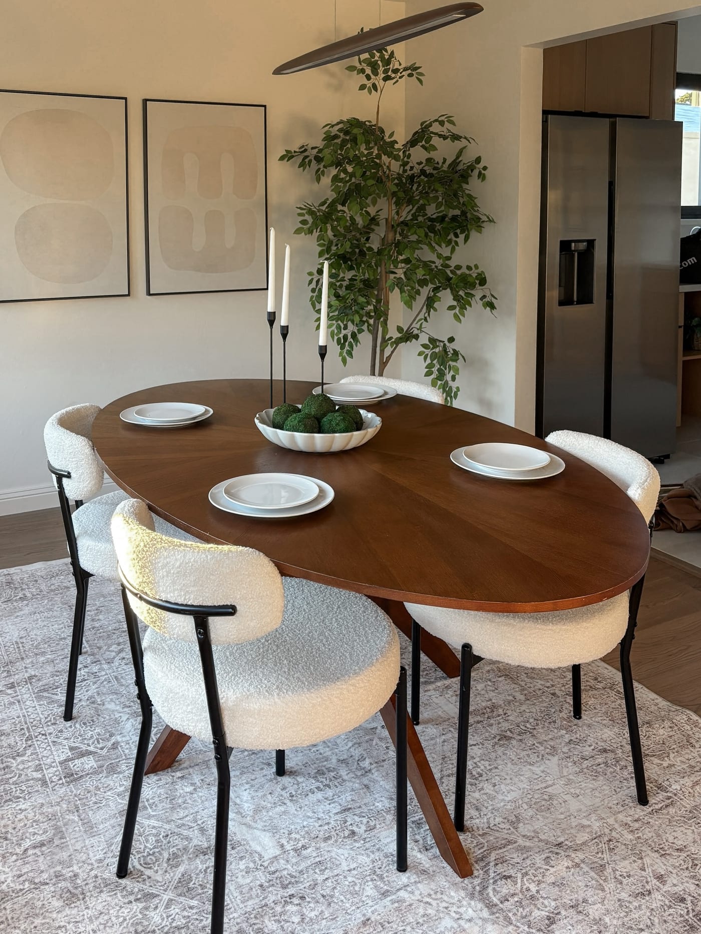 Staged dining room with a walnut oval table, boucle chairs, and an abstract diptych