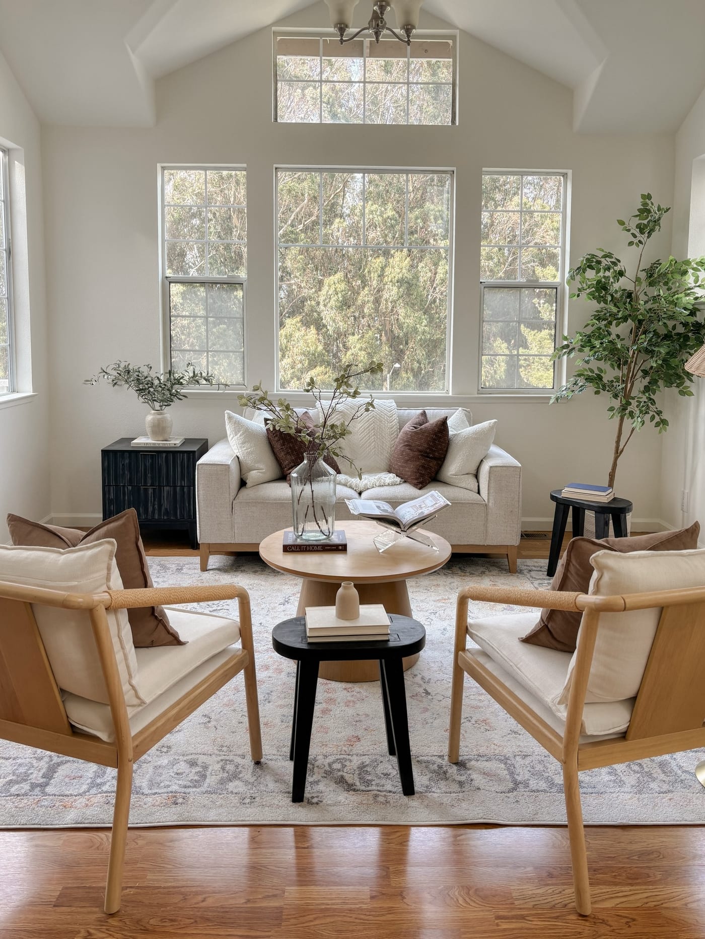 Bright staged living room with tall windows, a cream sofa, and cane armchairs