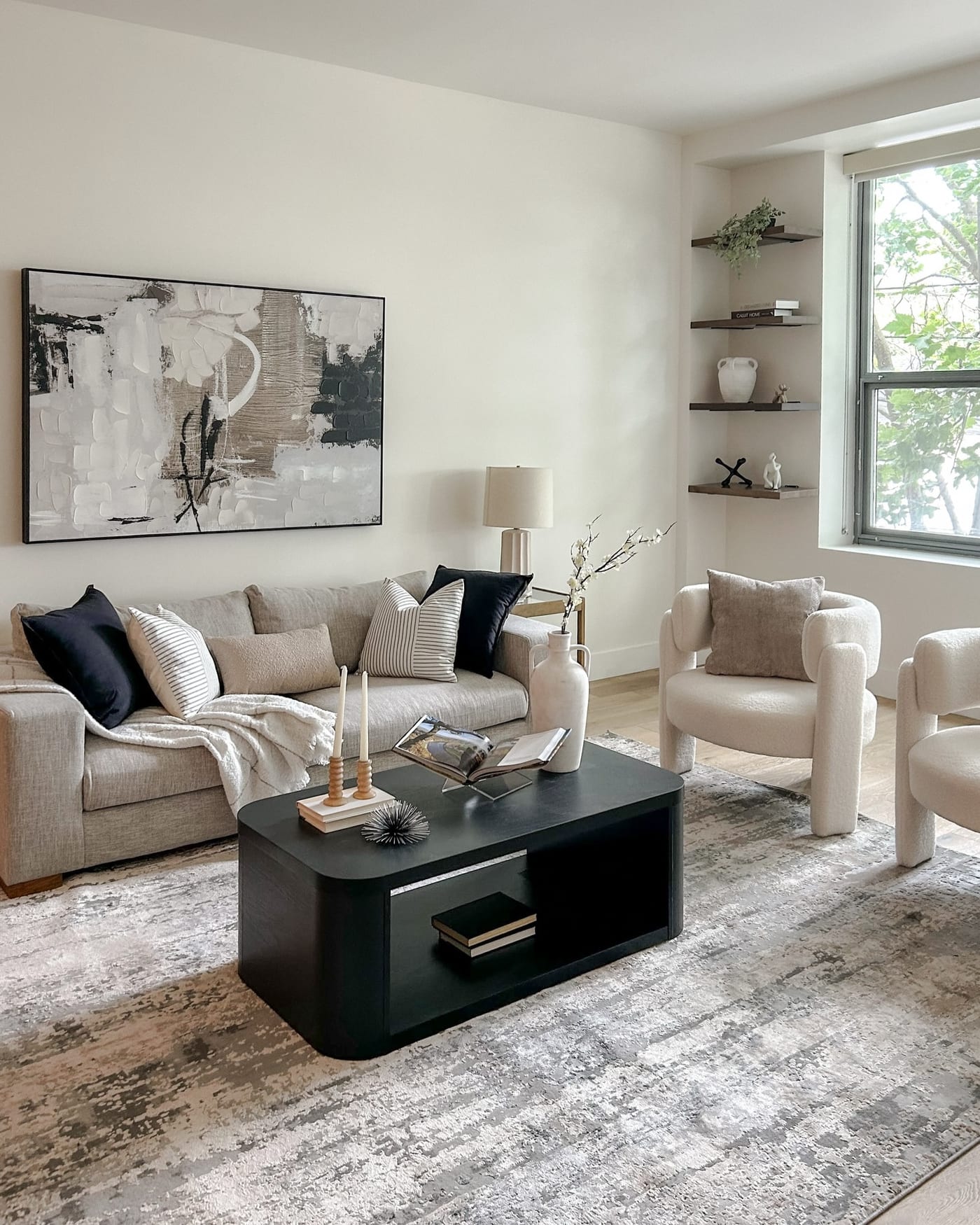 Staged living room with a cream sectional, boucle chairs, and a black oval coffee table