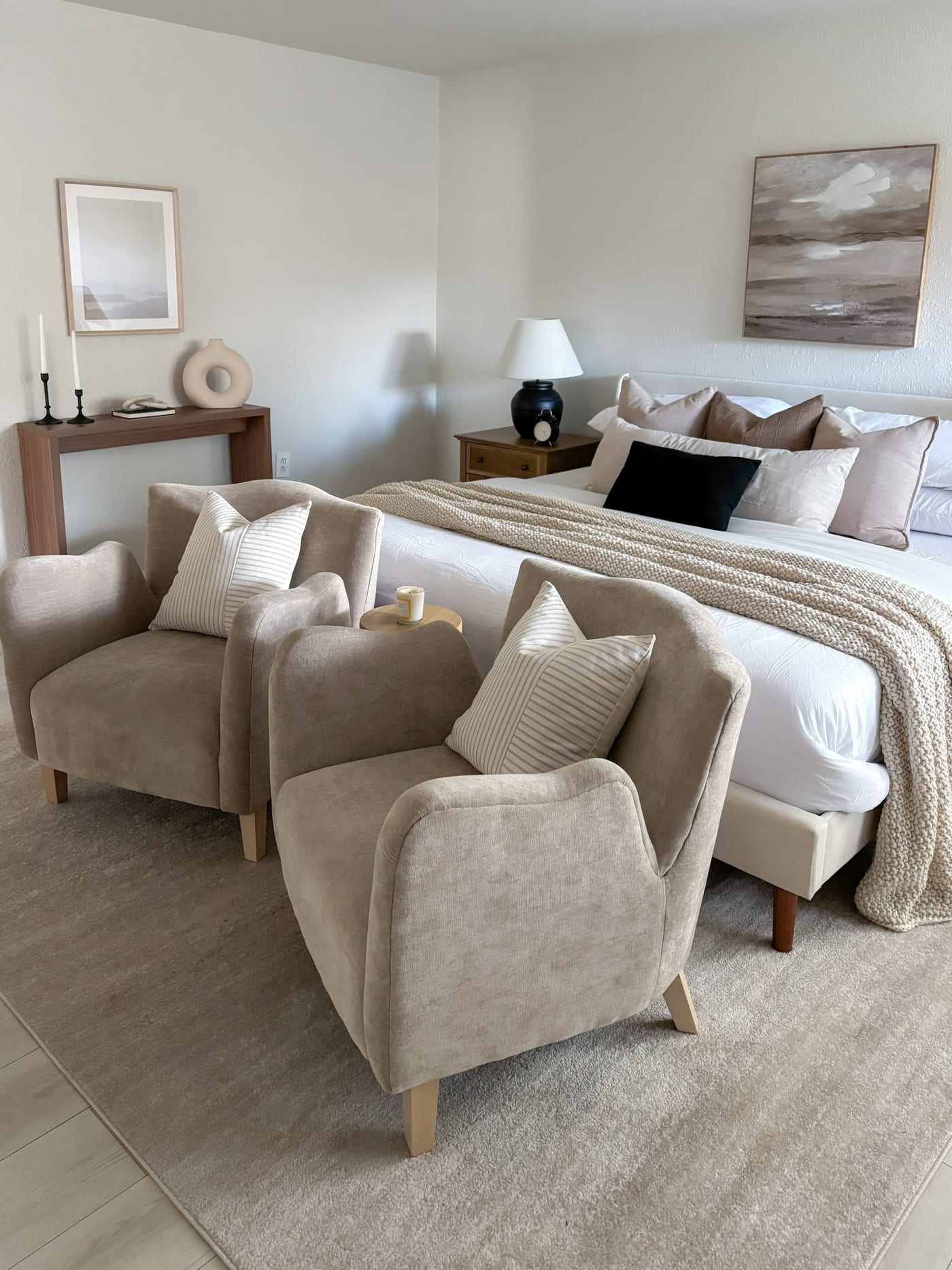 Staged primary bedroom with taupe accent chairs and a calm coastal palette