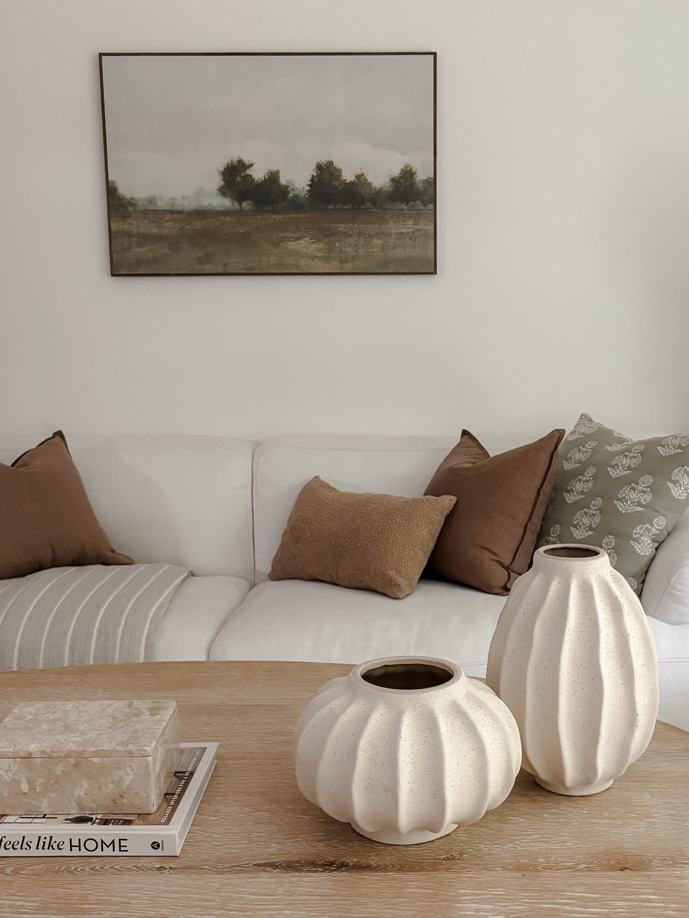 Staged living room with a white sofa, warm brown pillows, and a landscape painting