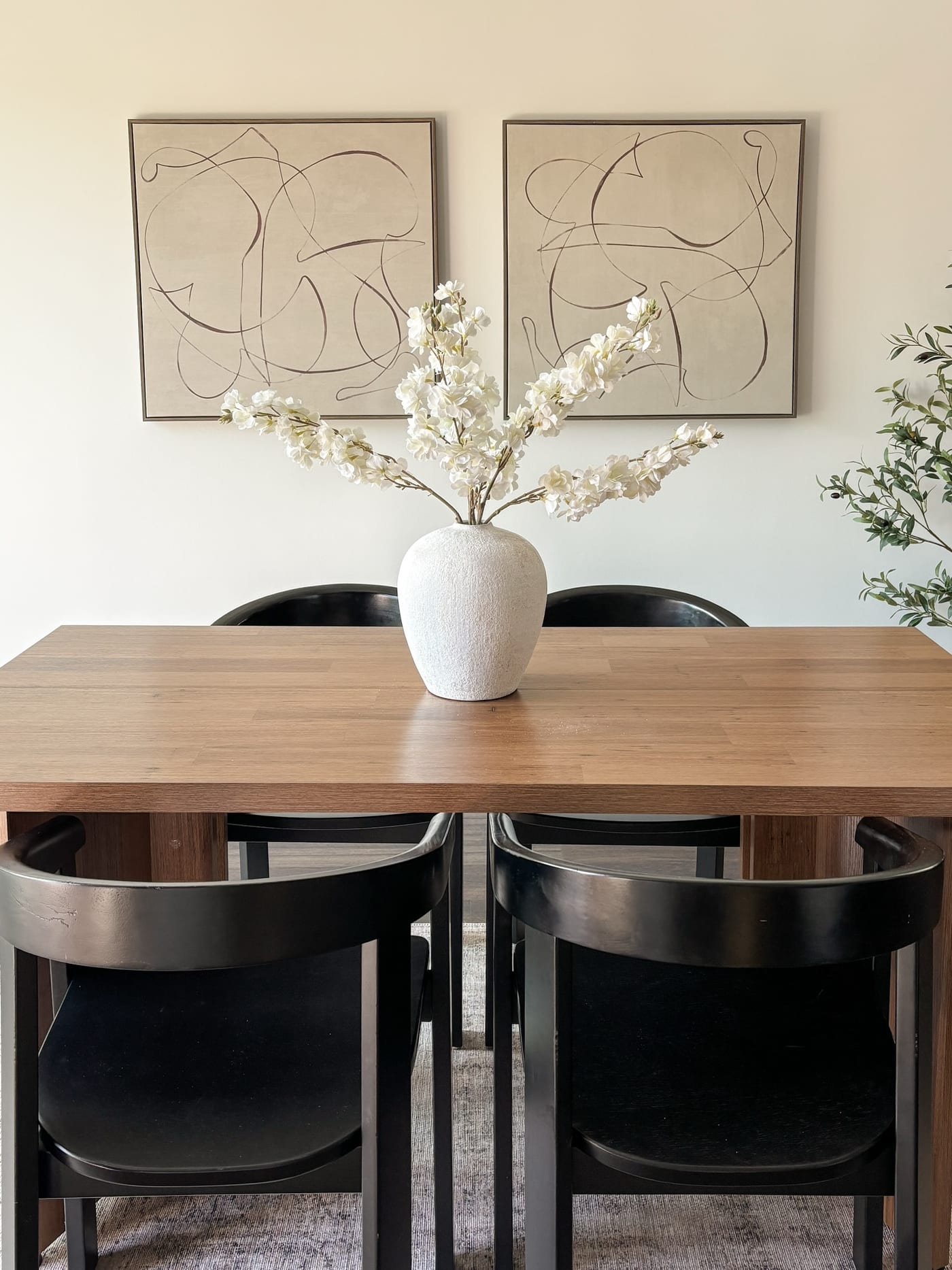 Staged dining room with a wood table, black chairs, and an abstract diptych
