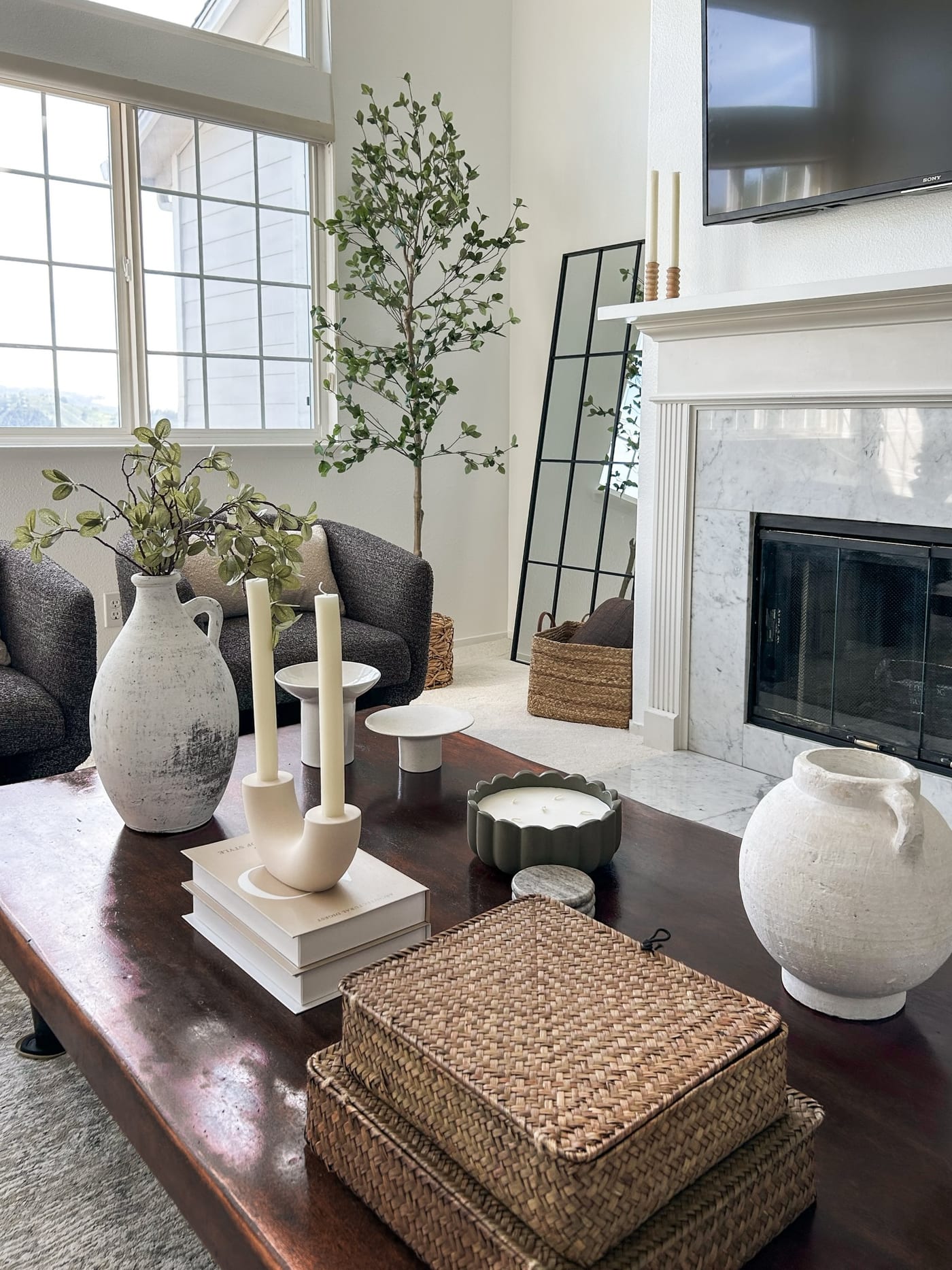 Staged living room with a marble fireplace, olive tree, and layered coffee-table styling
