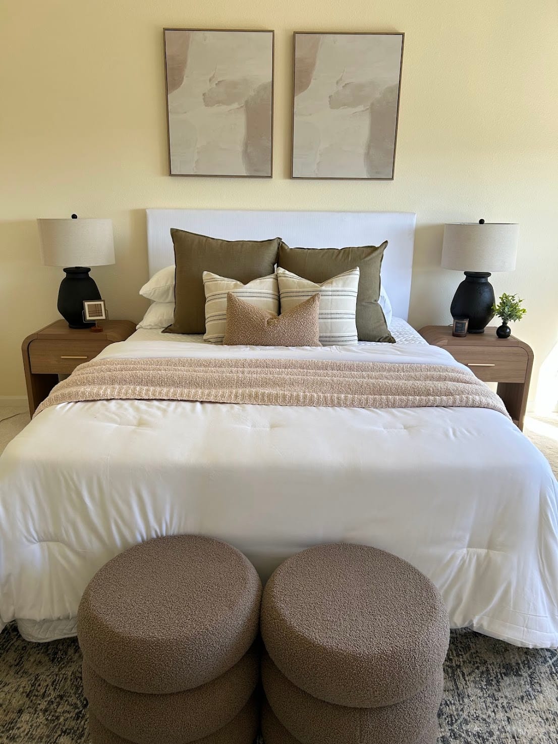 Staged bedroom with a white headboard, olive accents, and boucle poufs