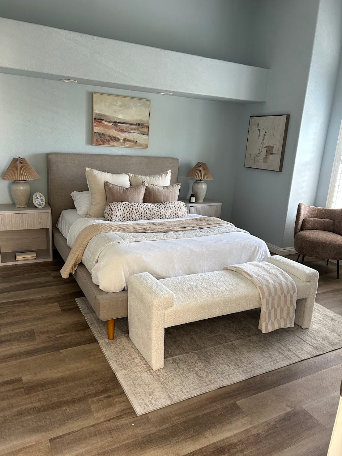 Staged primary bedroom with an upholstered bed, boucle bench, and landscape art