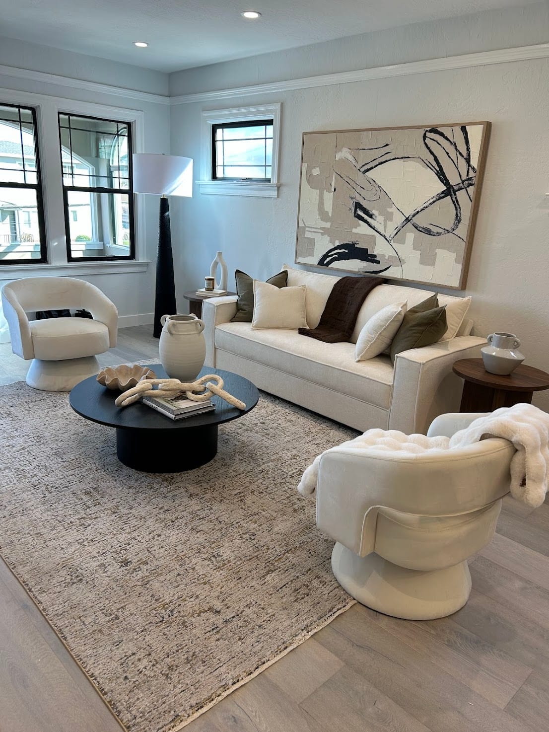 Staged living room with a cream sofa, boucle swivel chairs, and a large abstract canvas