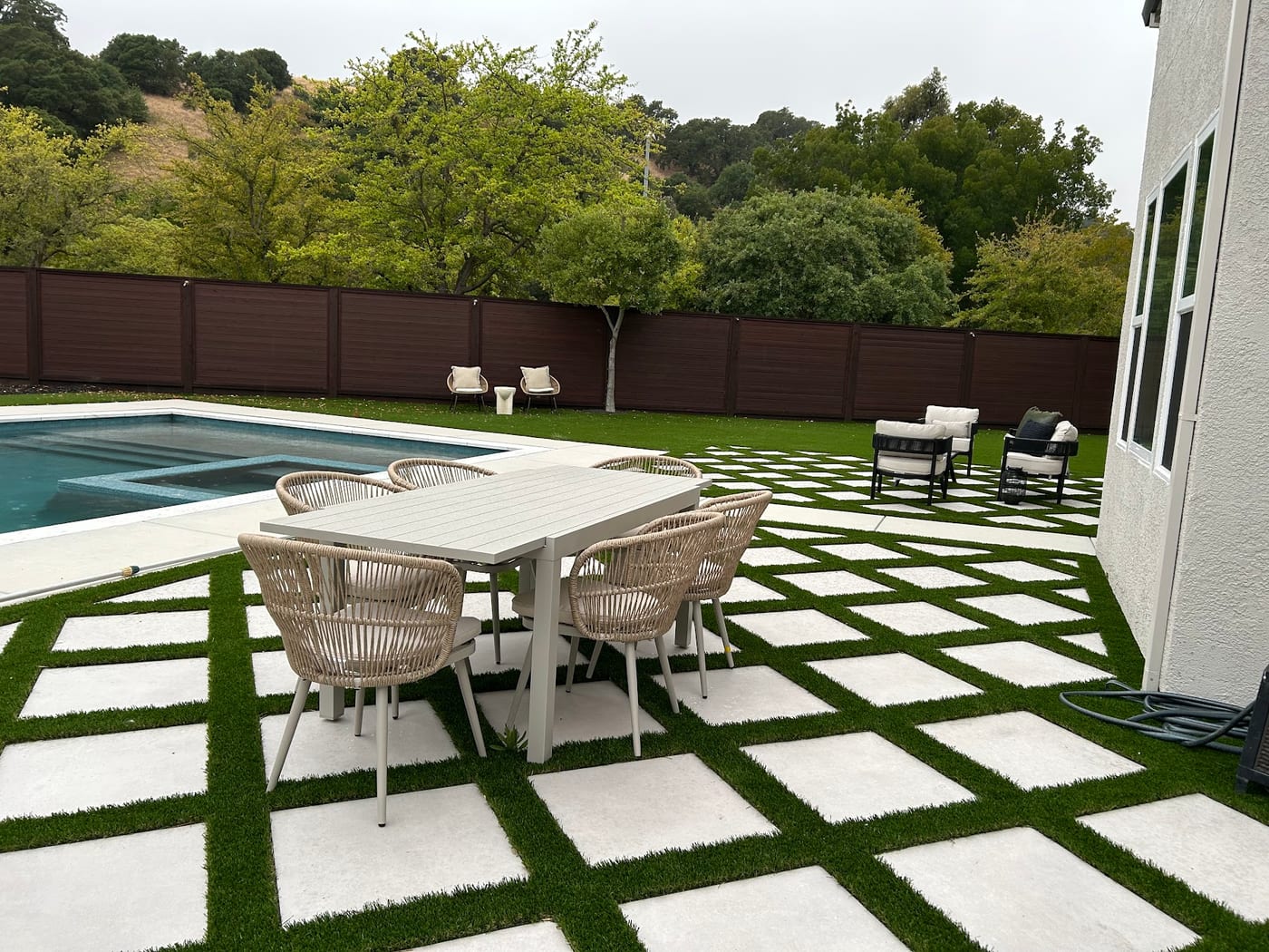 Staged backyard with a pool, outdoor dining set, and a turf-and-paver patio