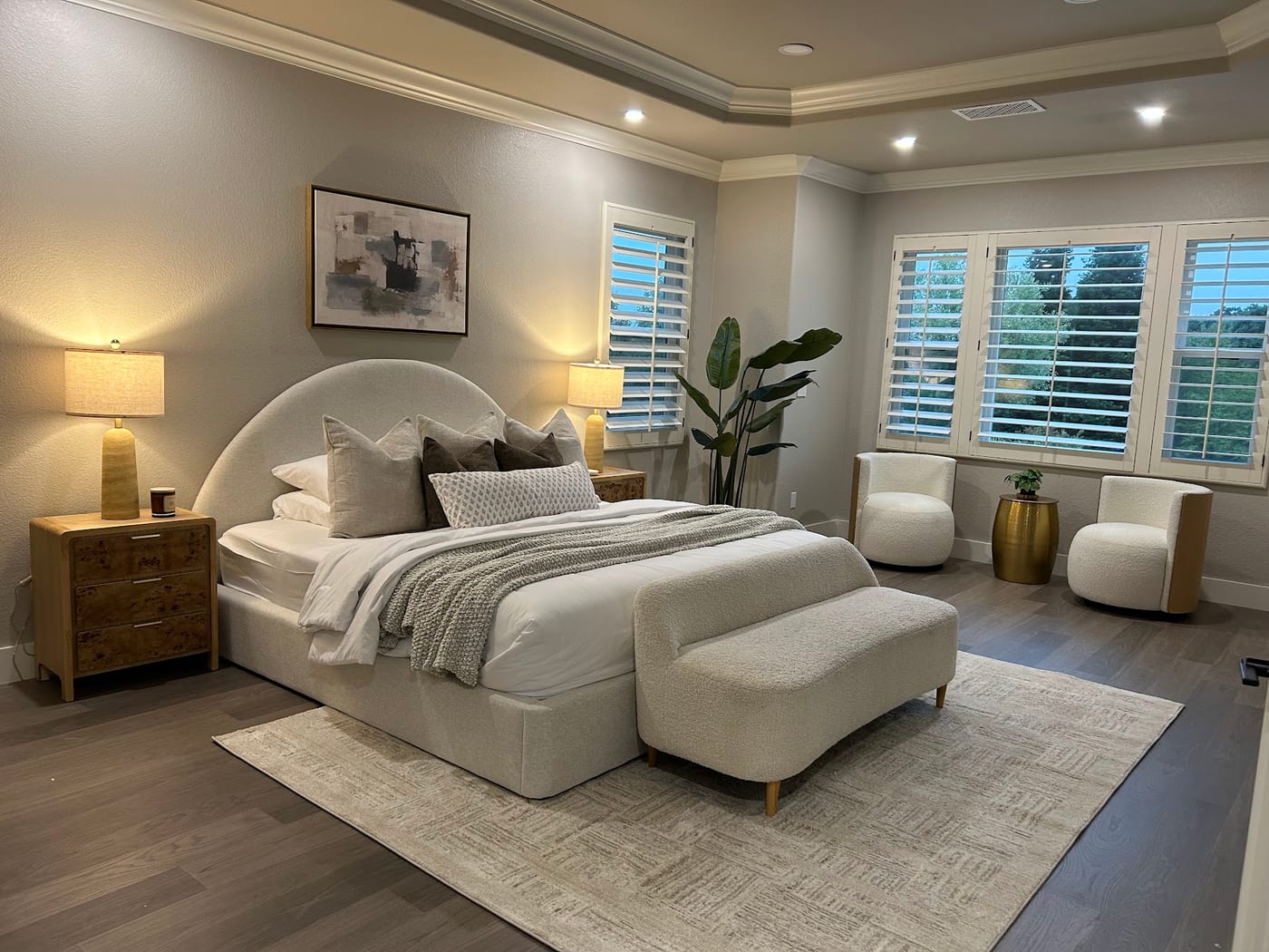 Staged primary suite with a tray ceiling, upholstered bed, and boucle seating