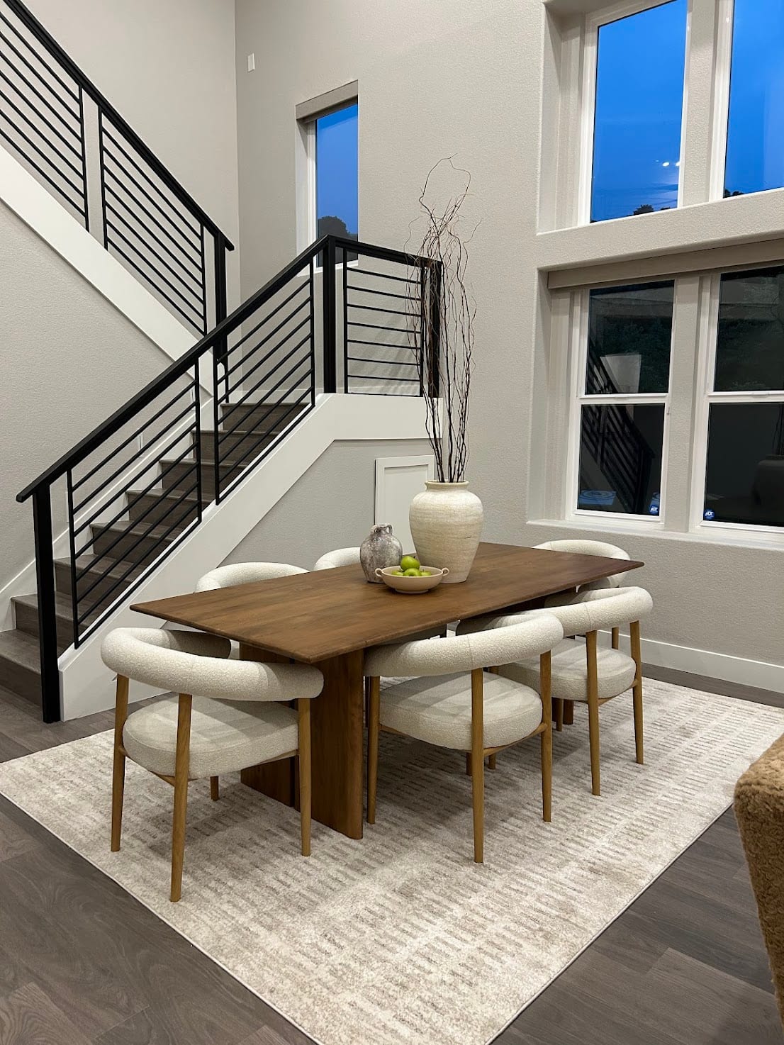 Staged dining area with a wood table, boucle chairs, and a modern staircase