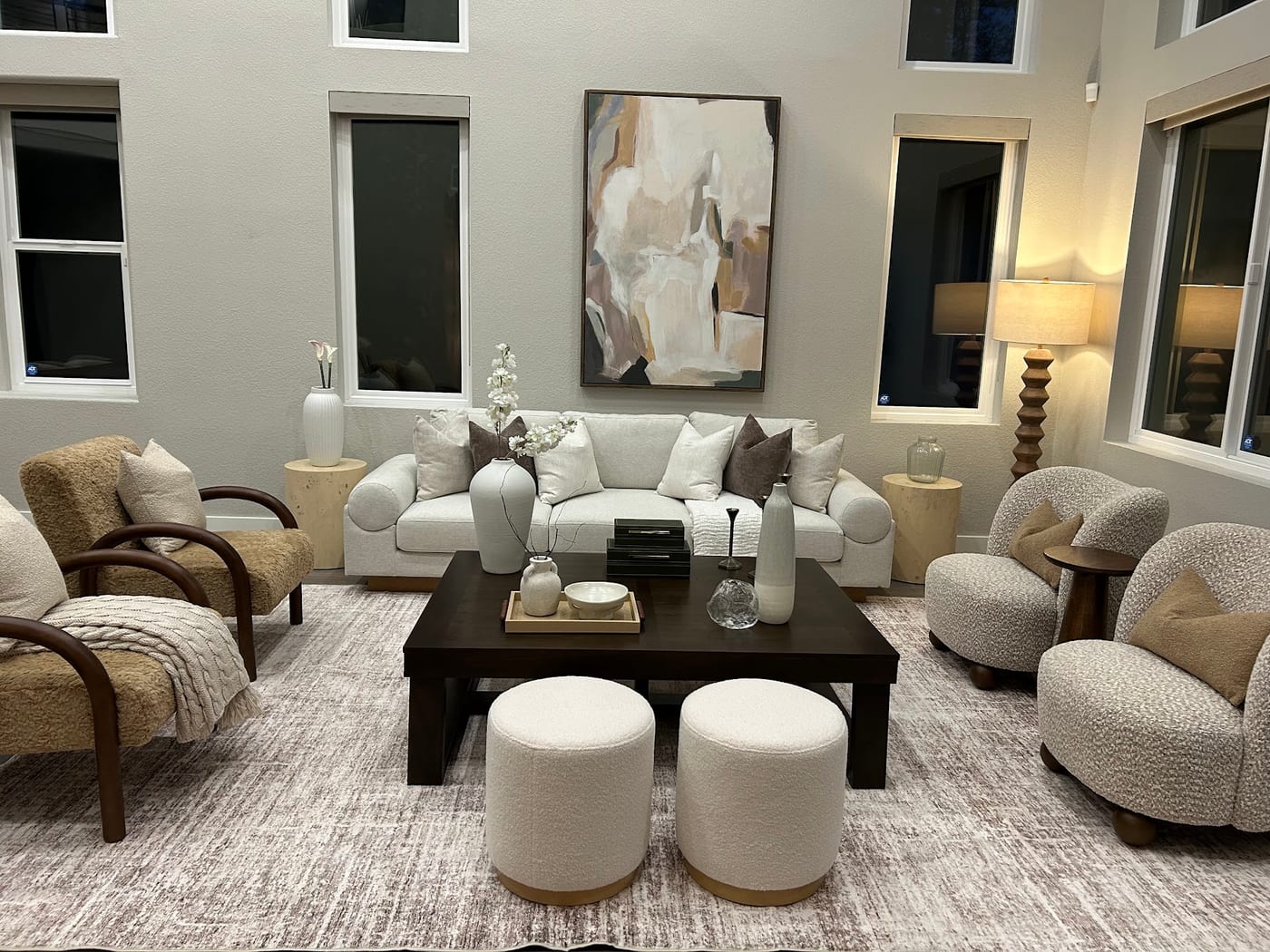 Staged living room with a cream sofa, boucle poufs, and soaring ceilings