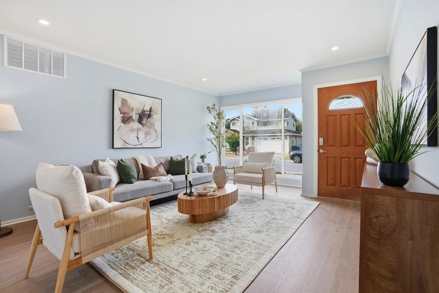 Staged living room by the entry with a grey sofa, cane chair, and warm wood door