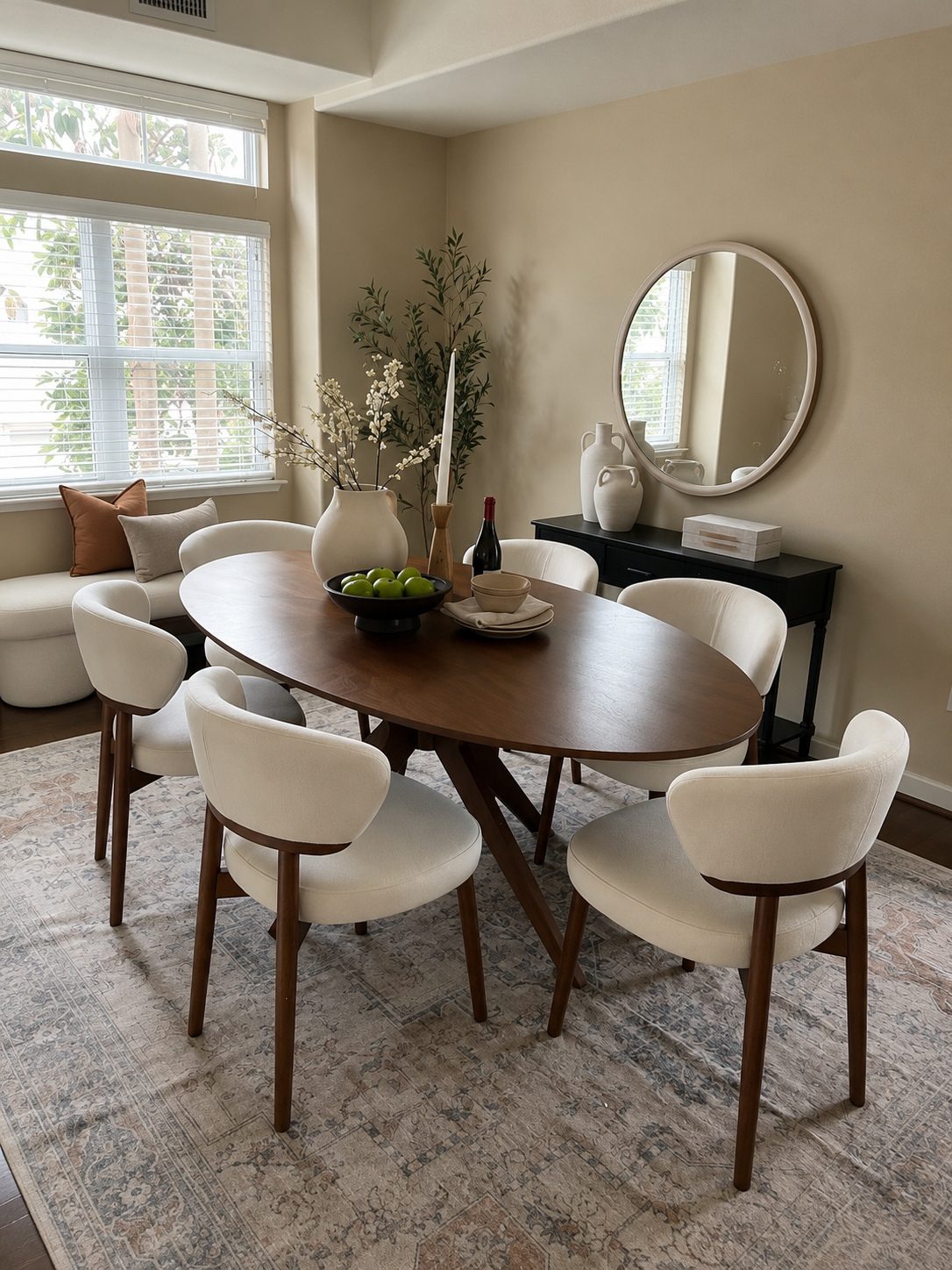 Staged dining room with a walnut oval pedestal table, cream boucle chairs, a round mirror, and a black console