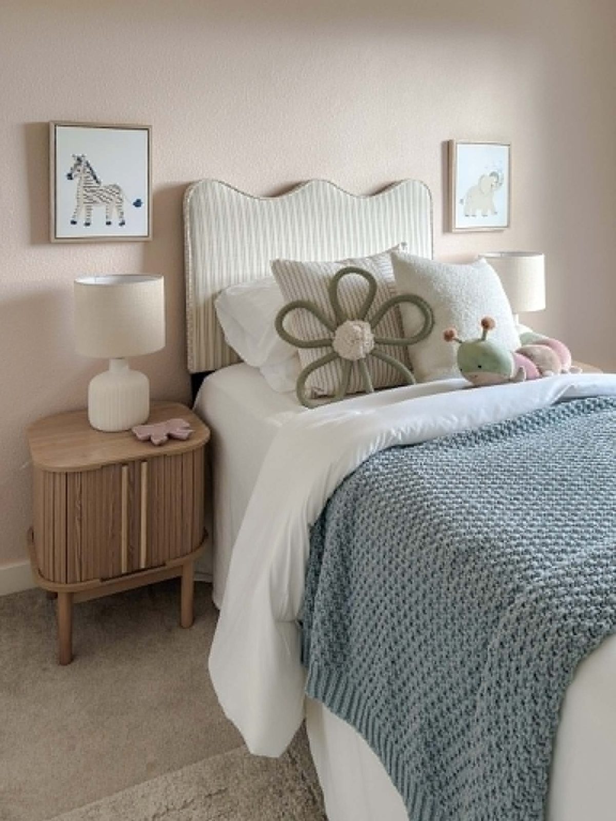 Staged children's bedroom with a scalloped striped headboard, a fluted-oak nightstand, a chunky teal knit throw, and framed animal prints